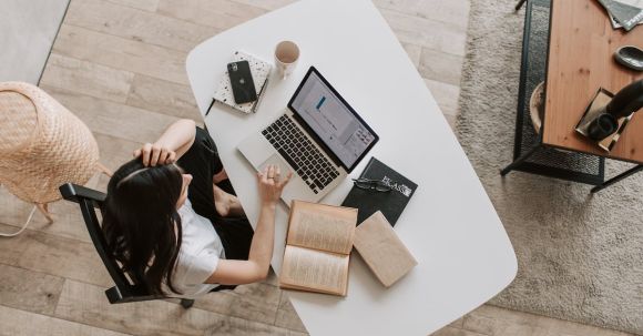 Job Search Motivation - From above of young woman with long dark hair in casual clothes working at table and browsing netbook while sitting in modern workplace and touching hair