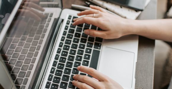 Job Search Balance - From above of unrecognizable woman sitting at table and typing on keyboard of computer during remote work in modern workspace