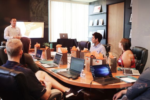 Job - man standing in front of people sitting beside table with laptop computers