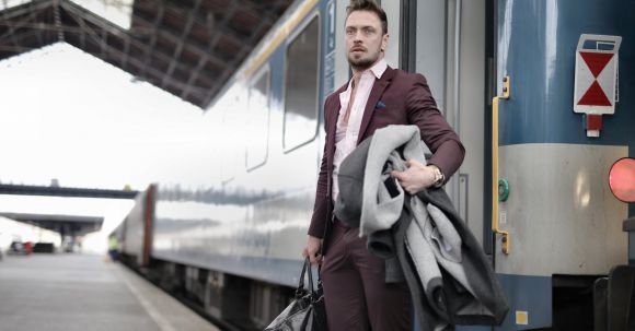 Career Transition Tips - Serious stylish bearded businessman in trendy suit holding bag and coat in hands standing near train on platform in railway station and looking away